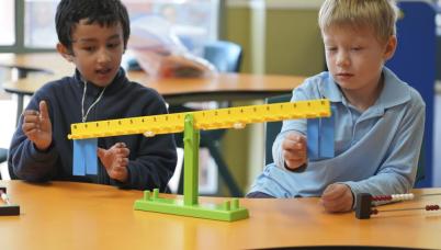 Two students examine a balancing tool. There is an abacus. 