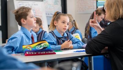 Students at their desk pay attention to a teacher. 