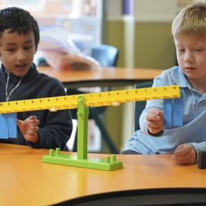 Two students examine a balancing tool. There is an abacus.