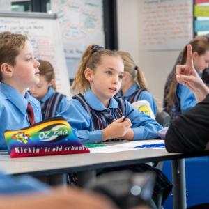 Students at their desk pay attention to a teacher.