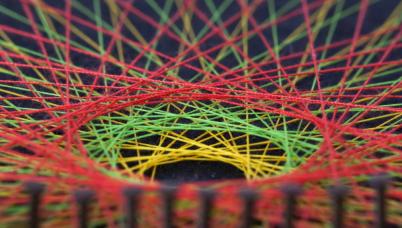Extreme close up of the centre of a piece of string art of multiple colours, aligned on nails
