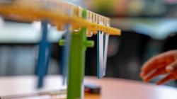 A plastic number balance on a desk, a student's hand reaching for it. 