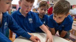 4 students participate in a balancing game at a desk. 