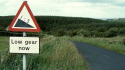 A rural road, signposted with a 1:5 warning and a 'Low gear now' sign. 